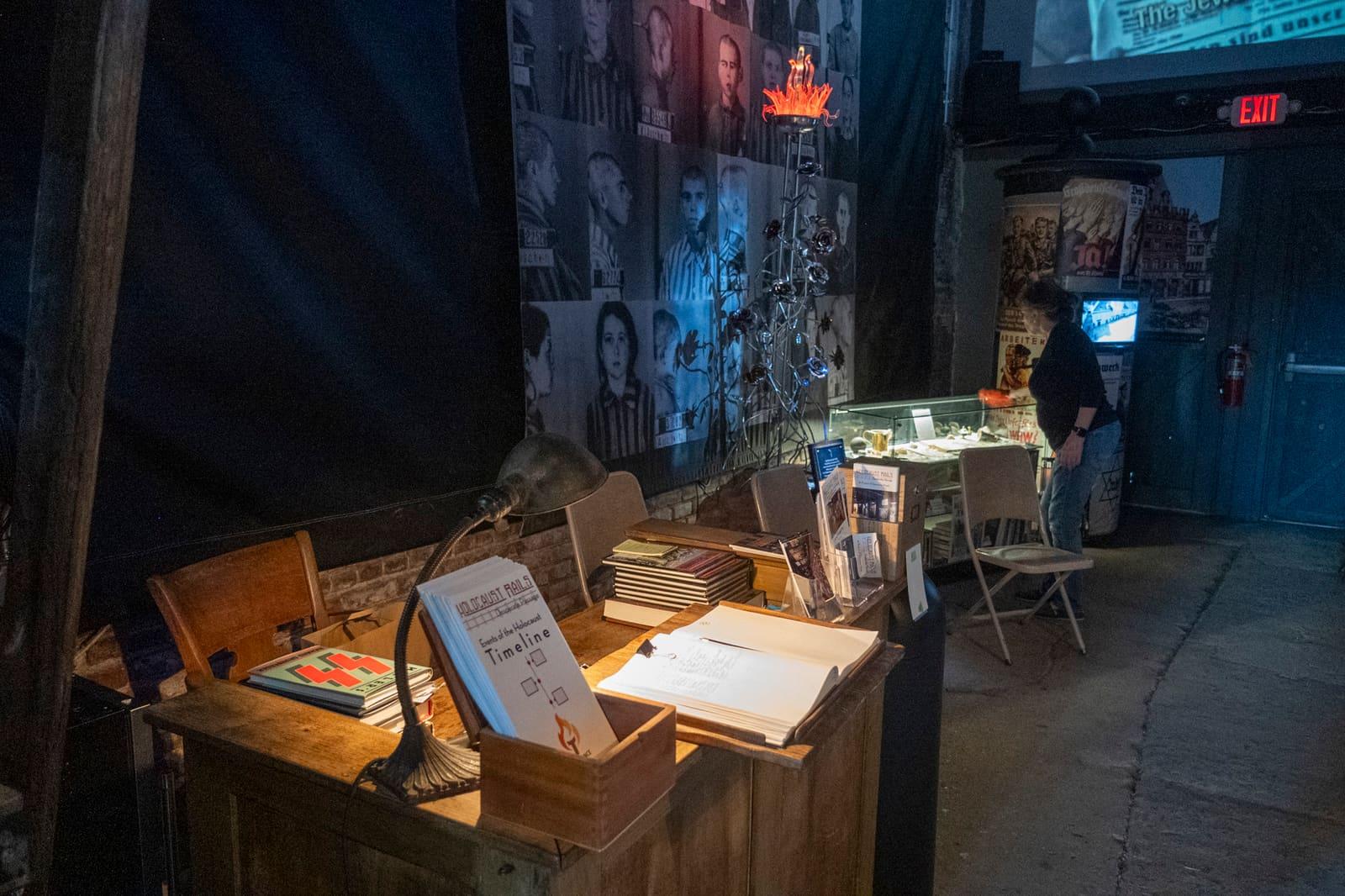 A wooden exhibit desk holds books, papers, and framed items.