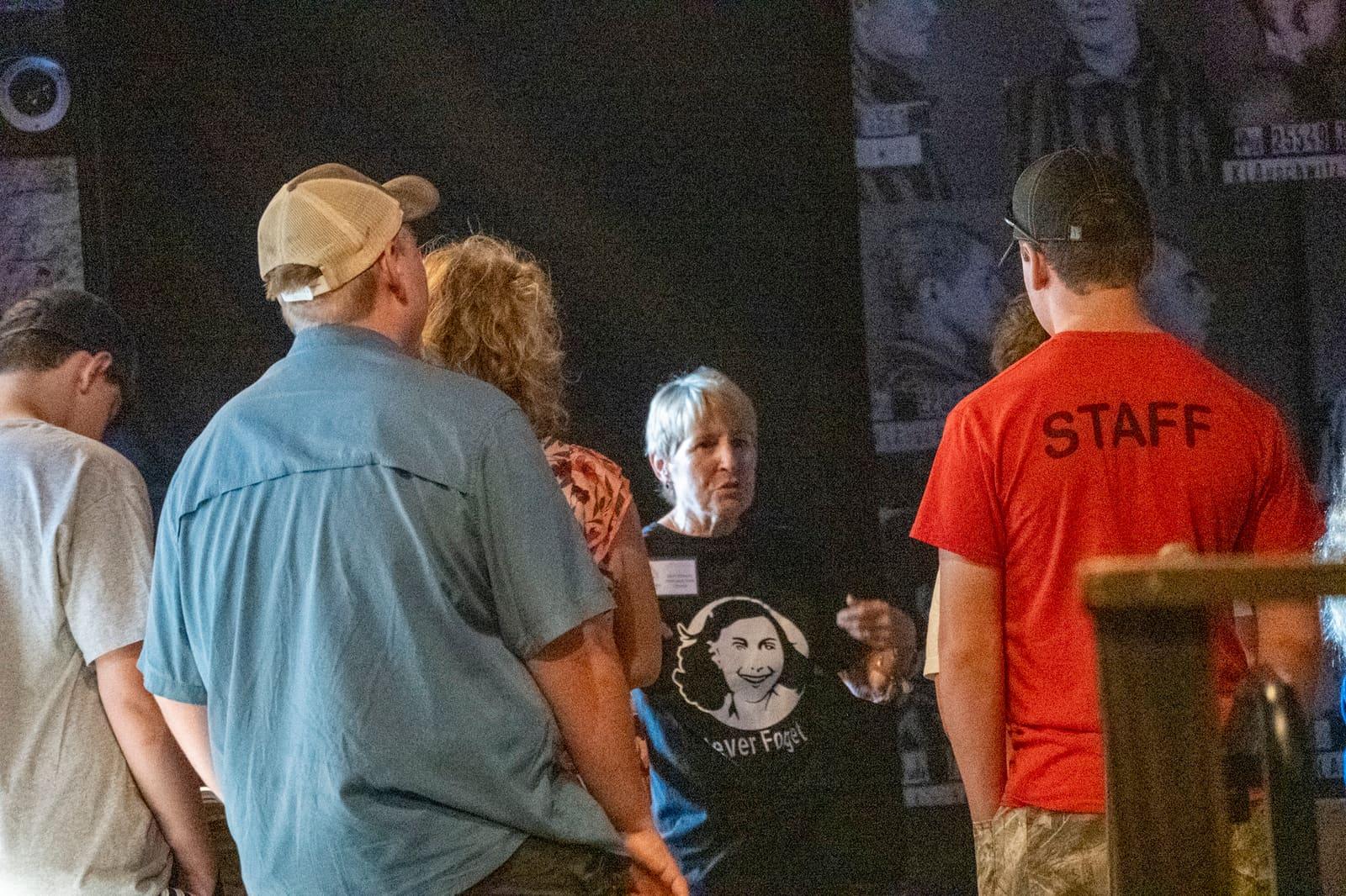 Visitors converse in a dim exhibit corridor beside a staff member.