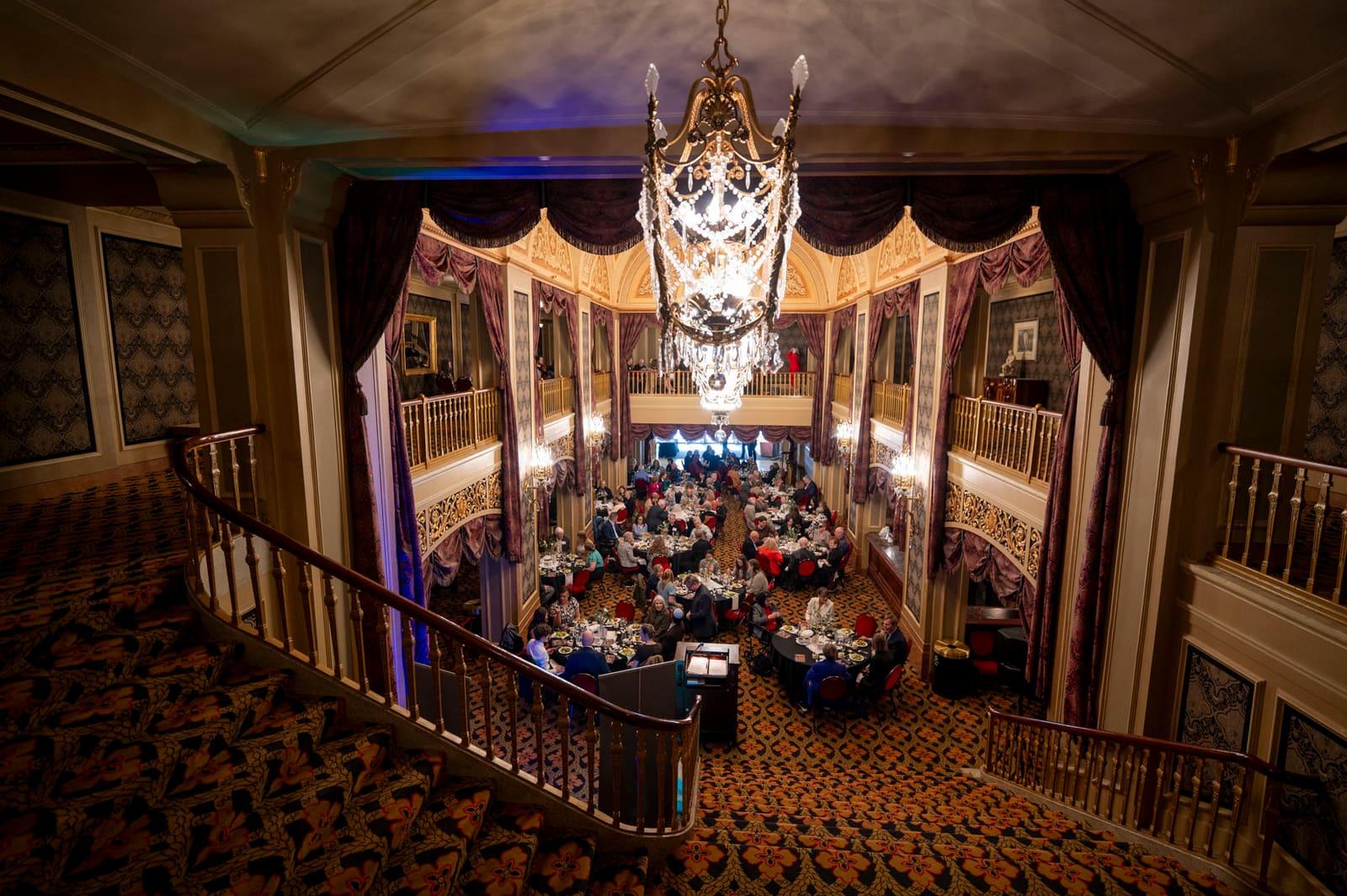 Banquet guests fill an ornate multi-level theater lobby.