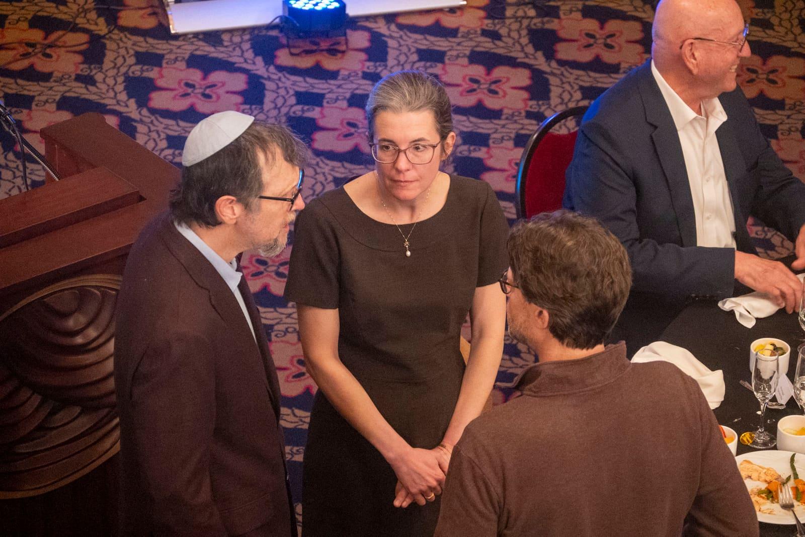 Three adults converse beside a banquet table.