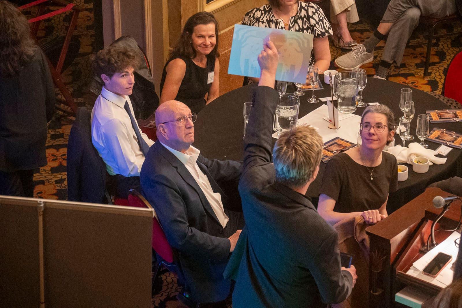 Adults gather around a seated guest at a banquet table.