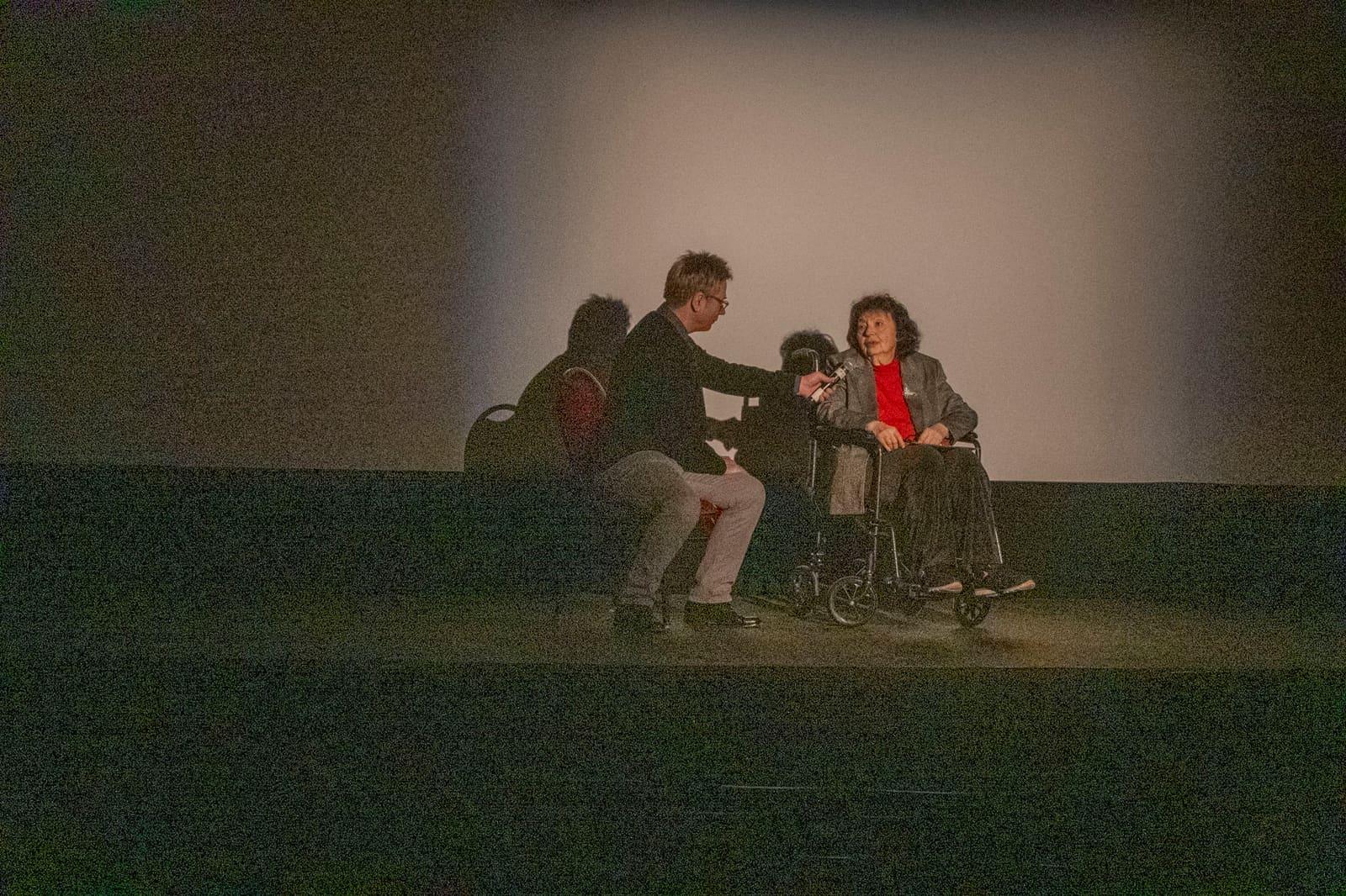 Three adults sit under a spotlight on an otherwise dark stage.