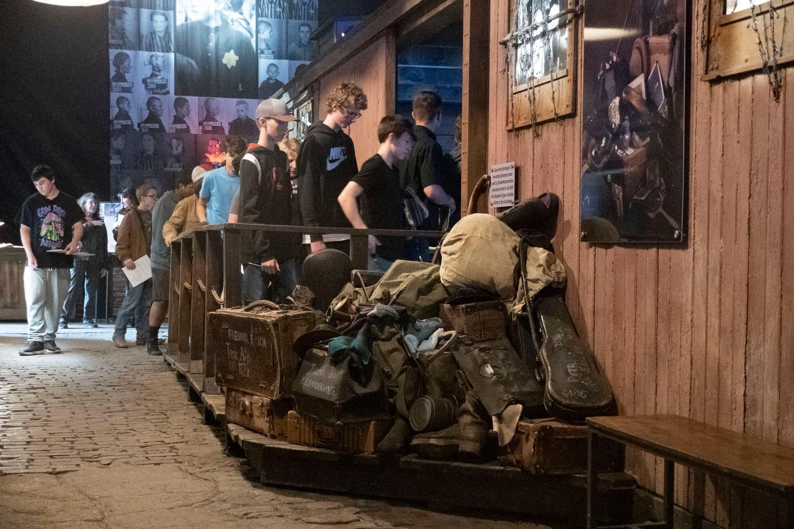 Visitors gather beside a large pile of worn luggage.