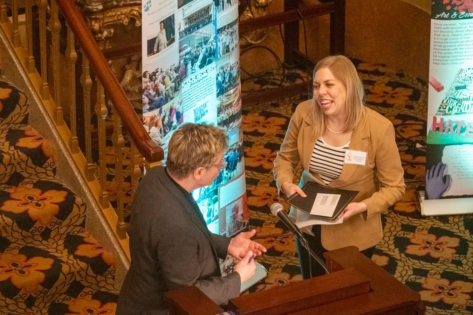 An adult hands a small item to an adult beside a lectern.