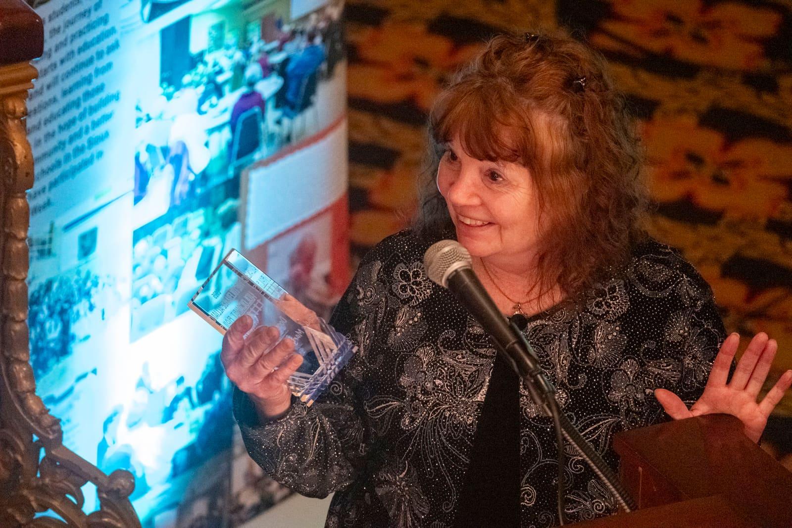 An adult gestures while holding a printed booklet.