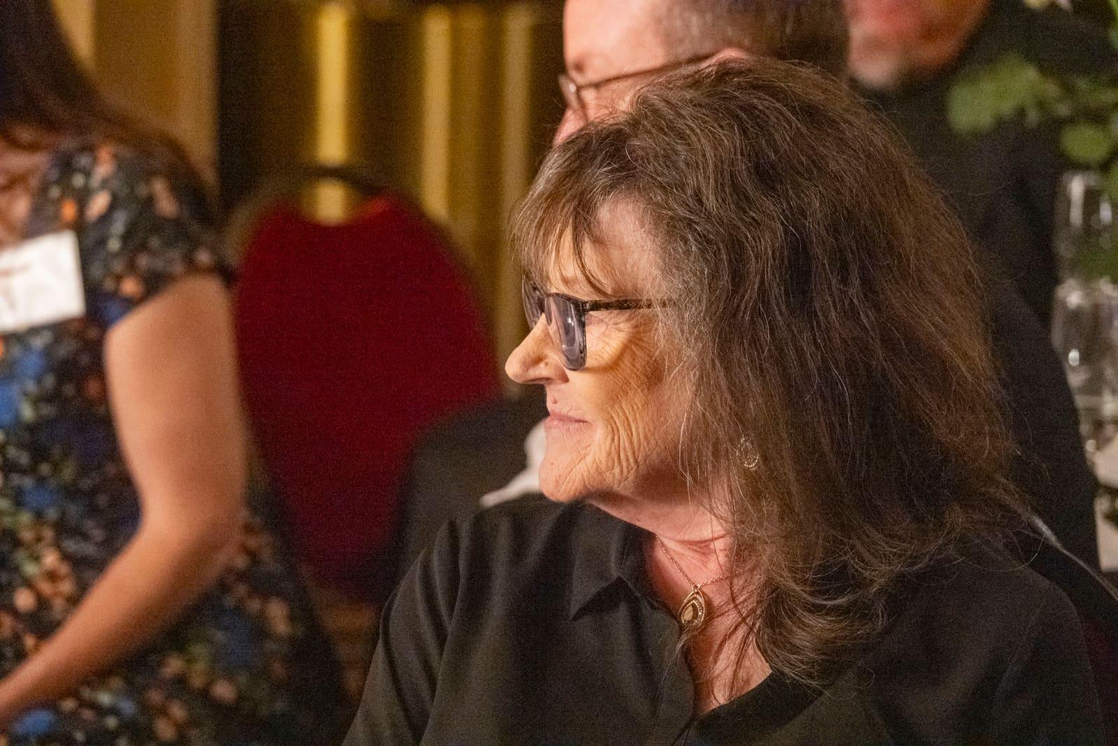 An adult with glasses sits at a banquet table.