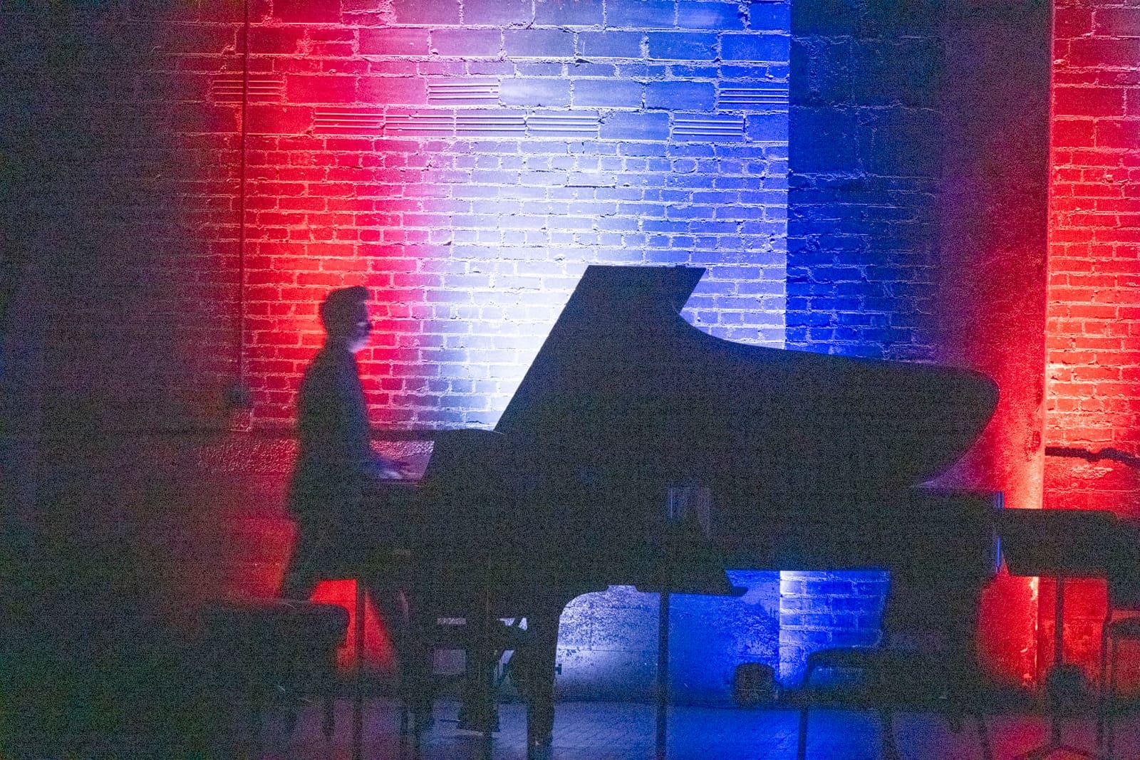 A pianist is silhouetted at a grand piano against red and blue light.