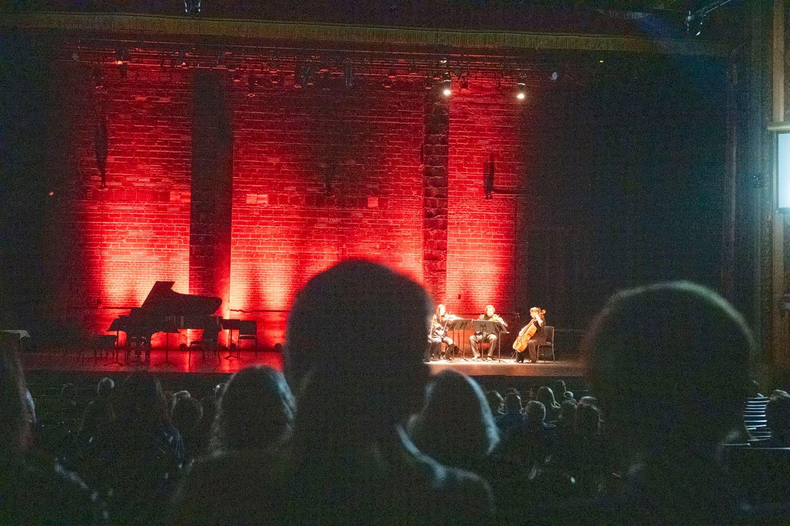 A pianist performs against a red-lit brick wall.