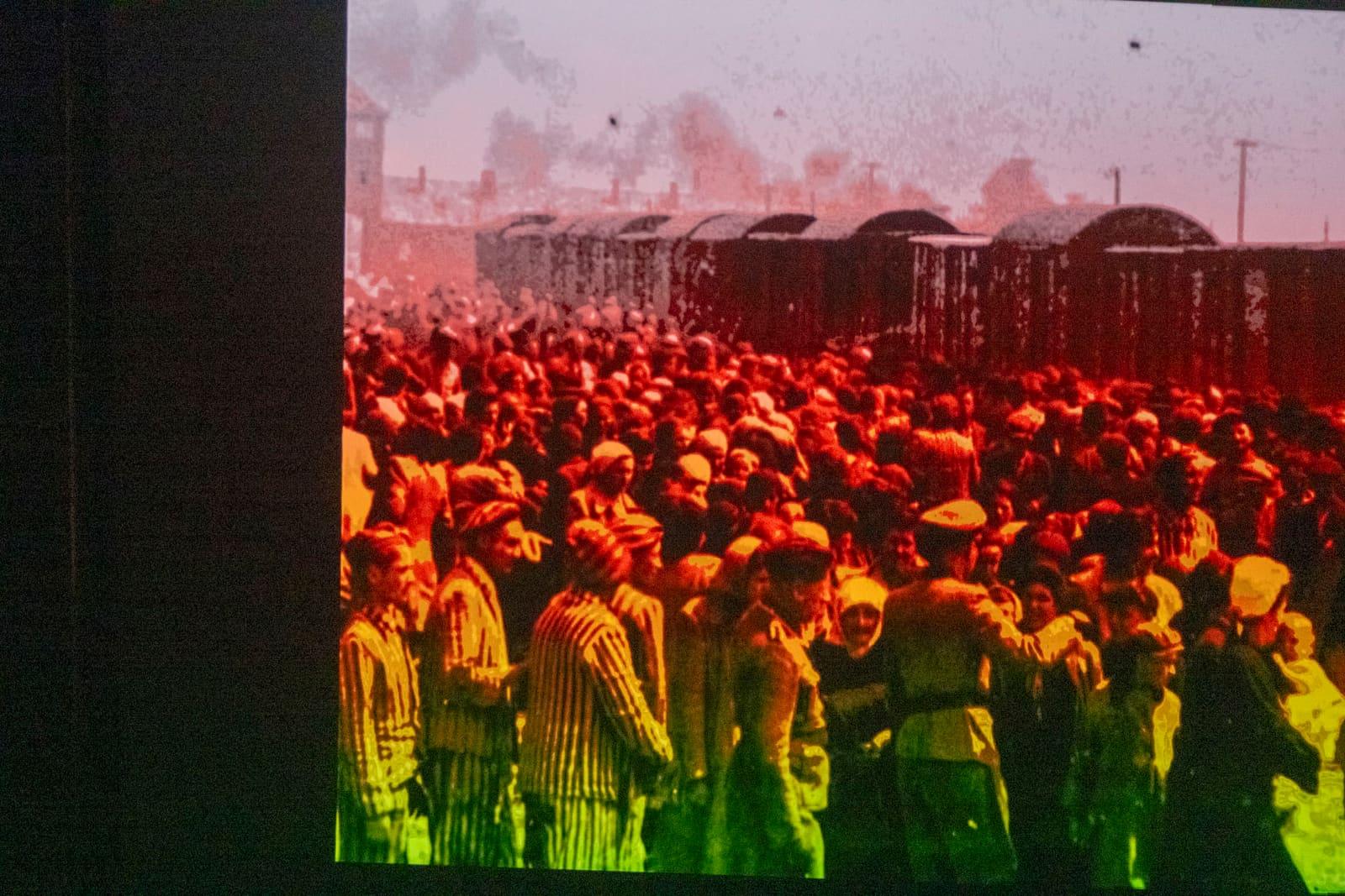A color-tinted historical image shows a dense crowd behind fencing.