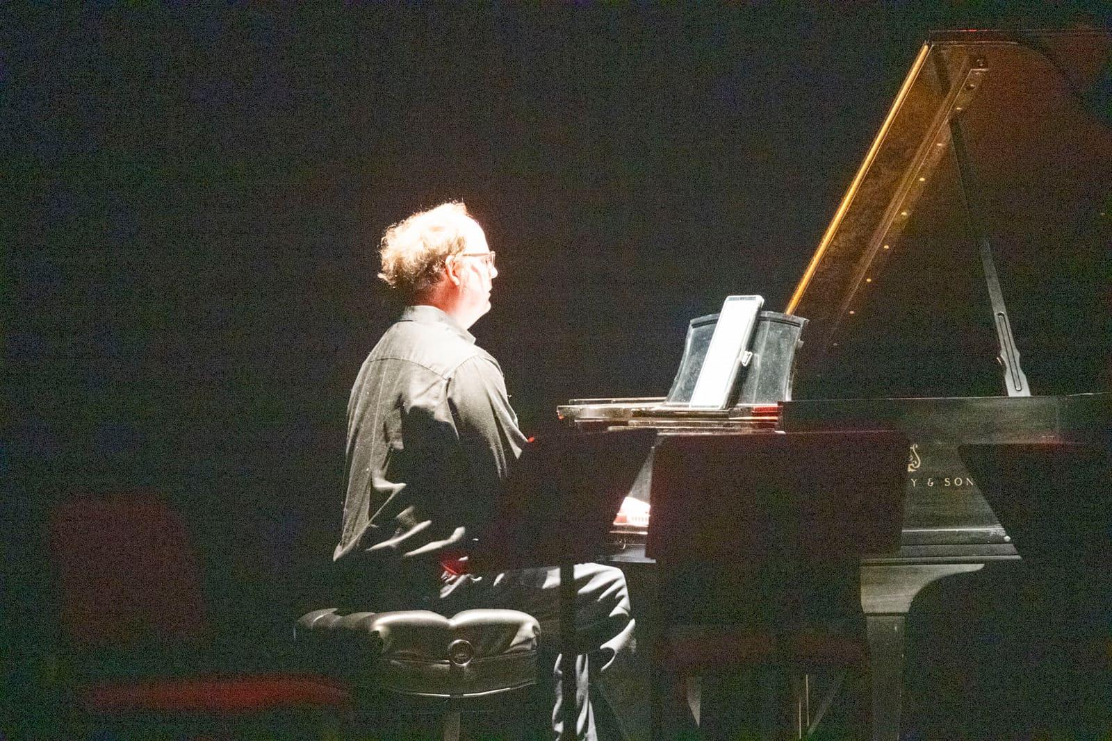 A pianist performs at a grand piano under a spotlight.