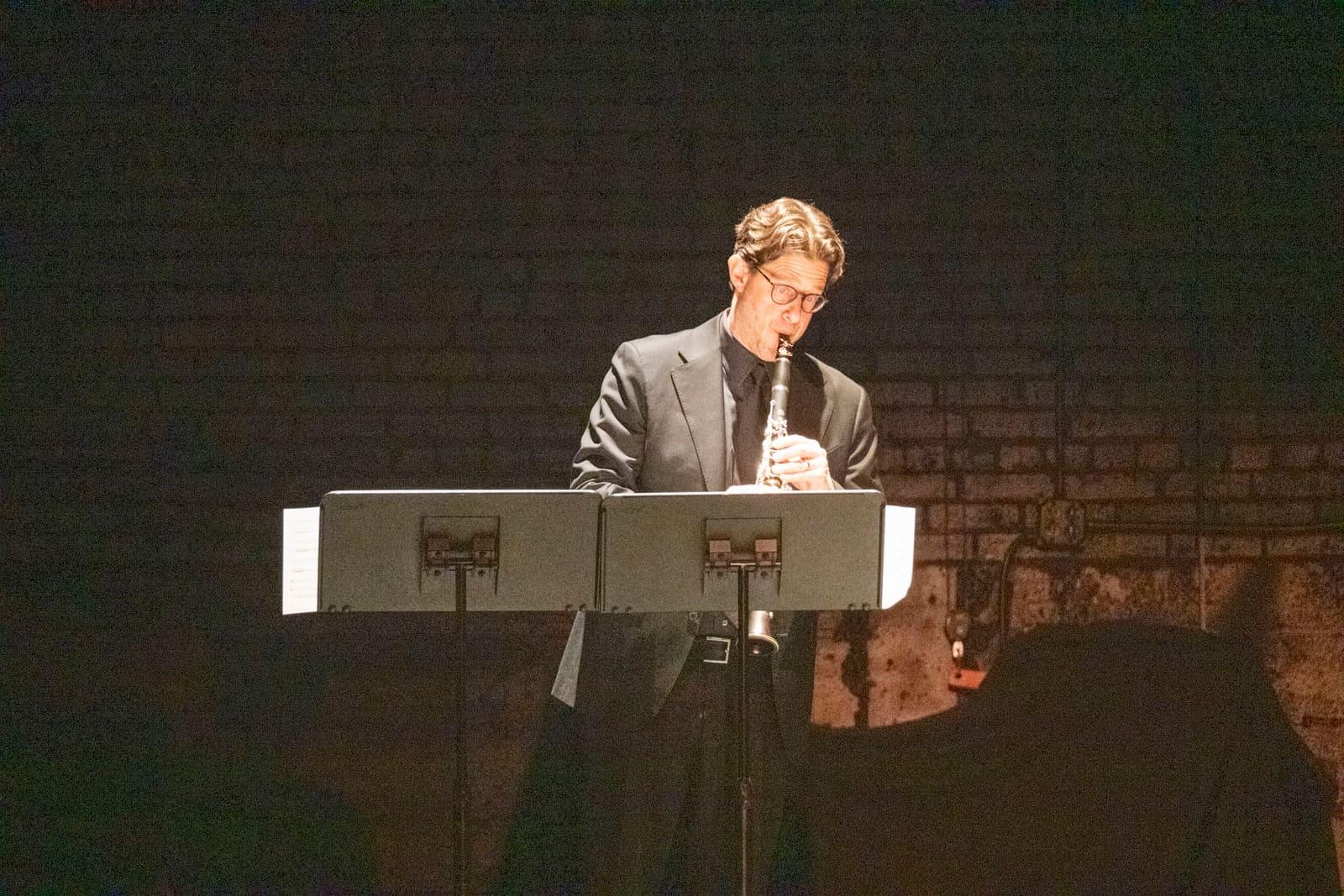 An adult performs behind an electronic keyboard on a dark stage.