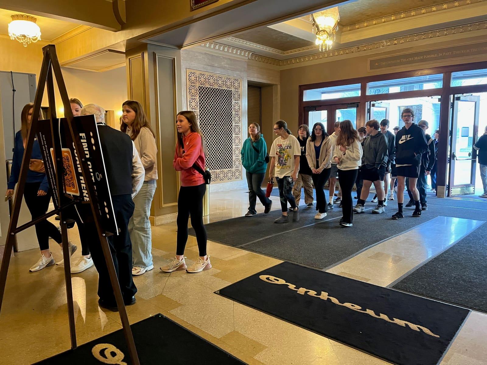Students line up in a lobby beside display easels.