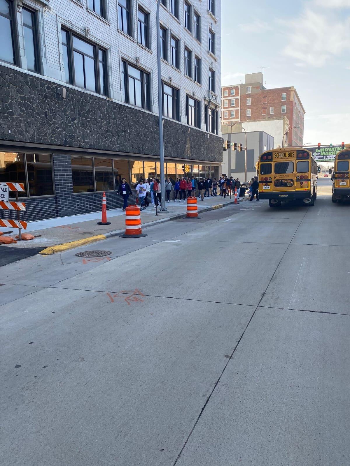 School buses travel on a city street between tall buildings.