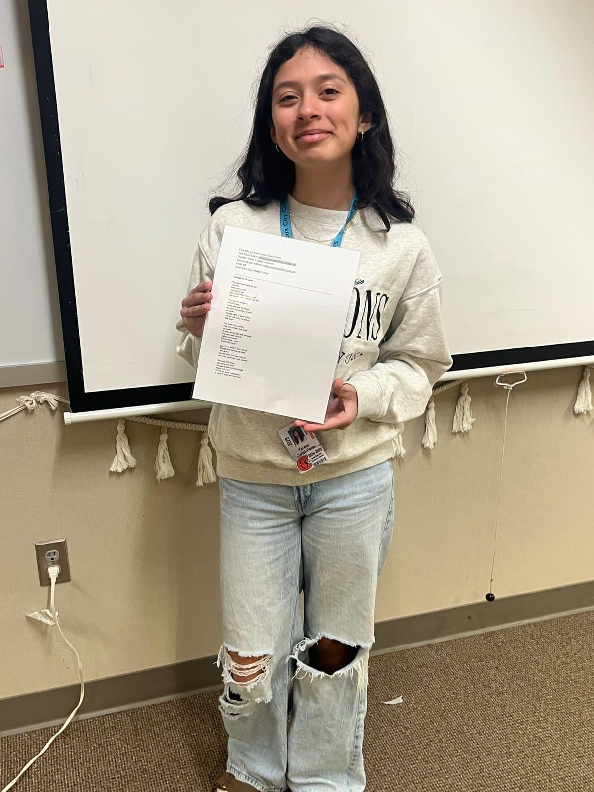 A student holds a certificate while standing in a classroom.