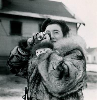 Black-and-white photograph of a smiling woman in a fur hood leaning backward outdoors.