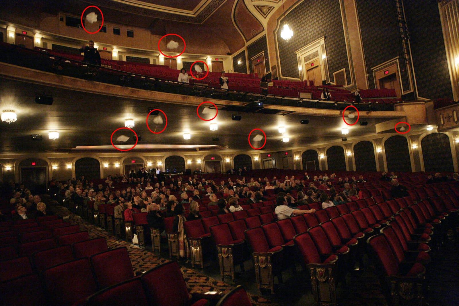 A theater audience faces the stage while red circles mark small parachutes around the balconies.