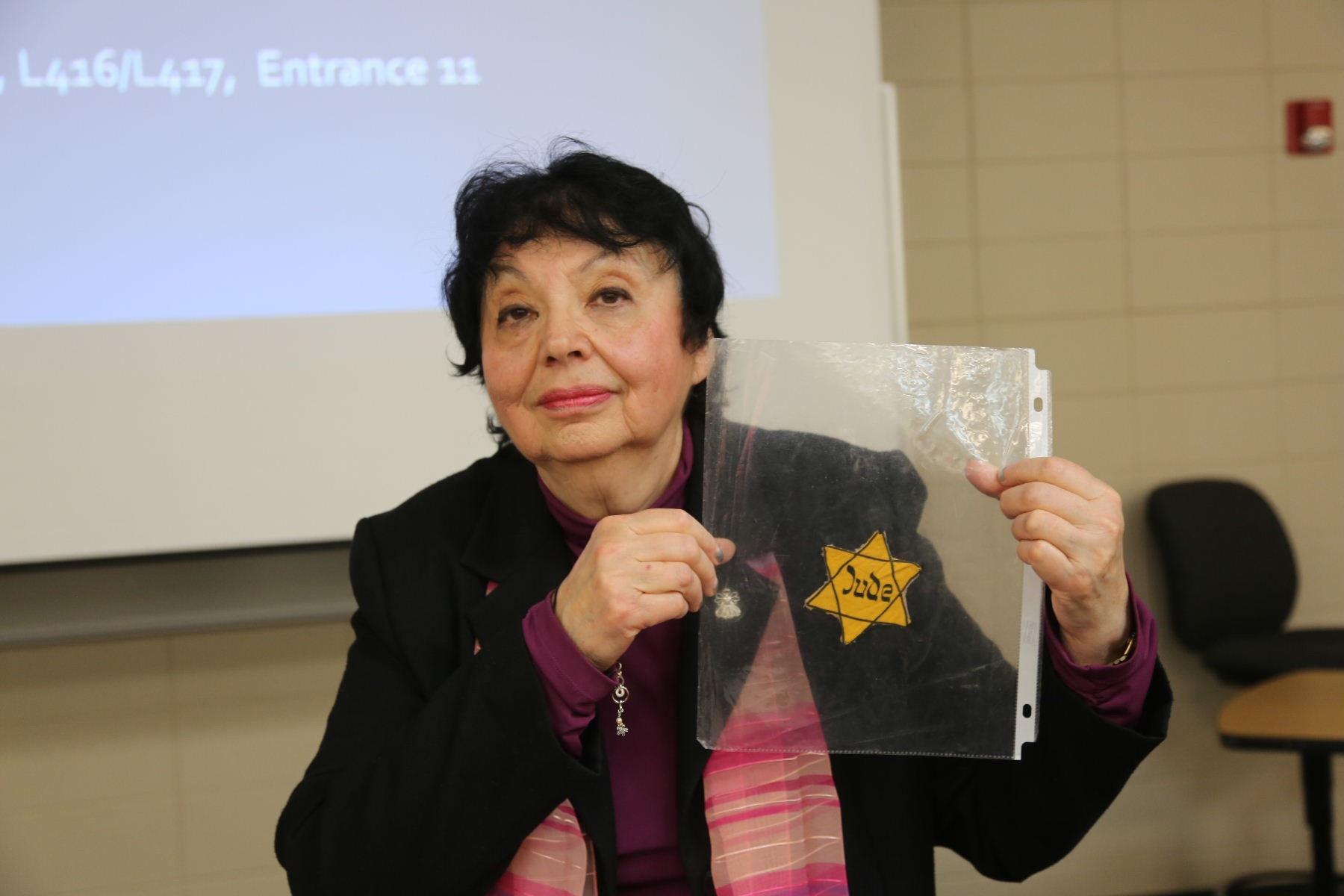 Inge Auerbacher holding a yellow Star of David badge marked "Jude" during an educational presentation